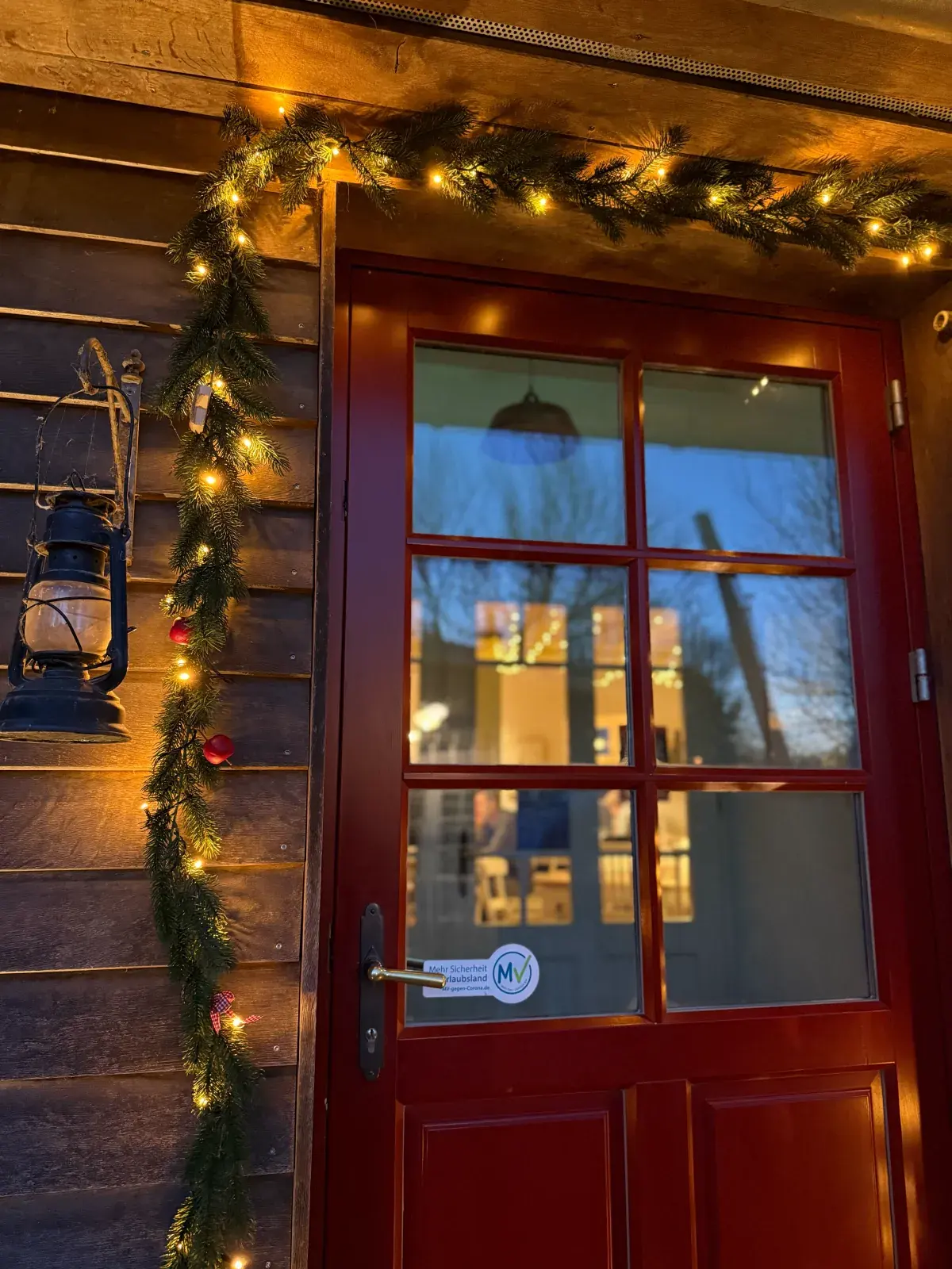 Die rote Tür der Mühle, weihnachtlich geschmückt mit Tannengirlande und Lichterkette