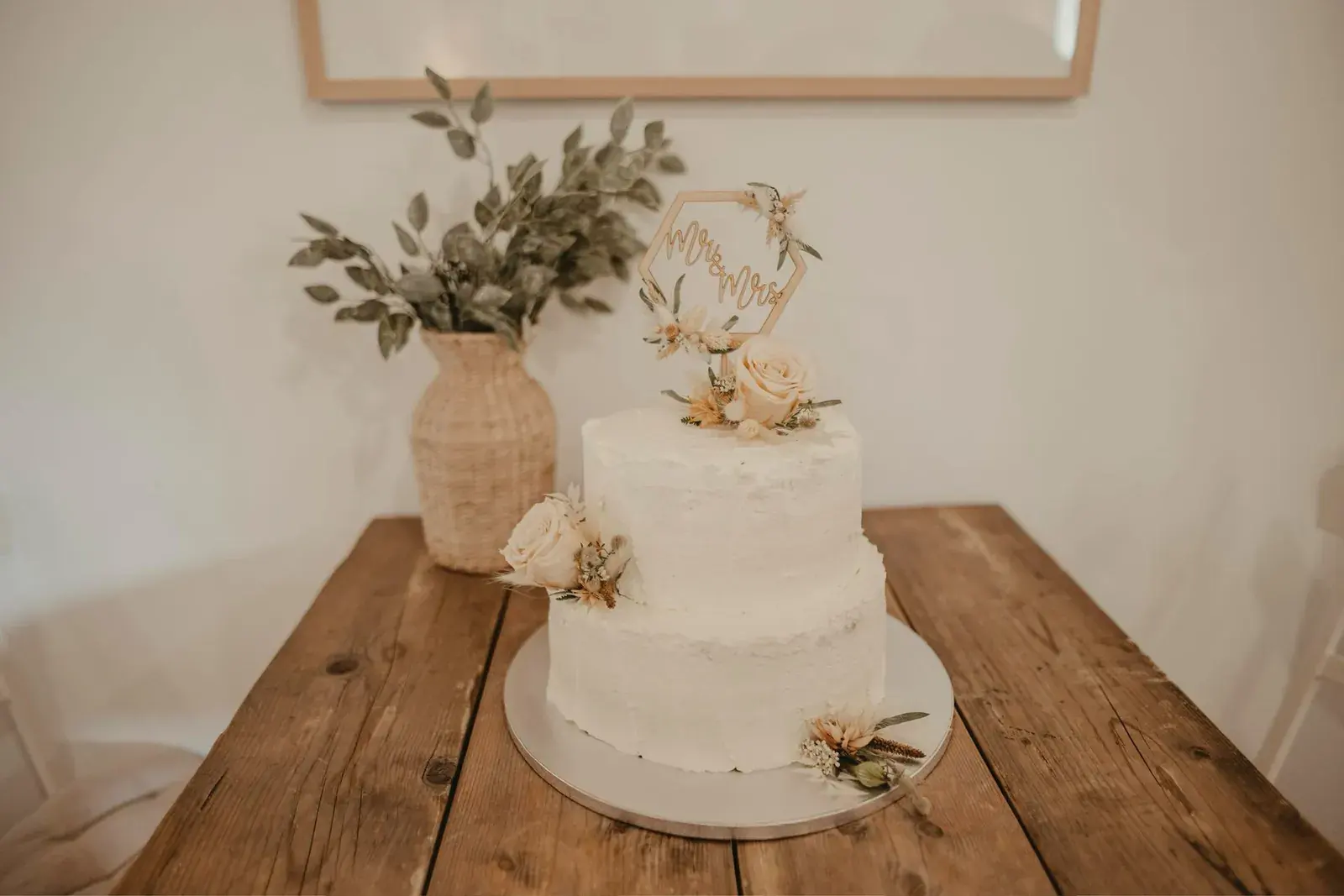 Zweistöckige weiße Torte mit Trockenblumen auf einem Holztisch