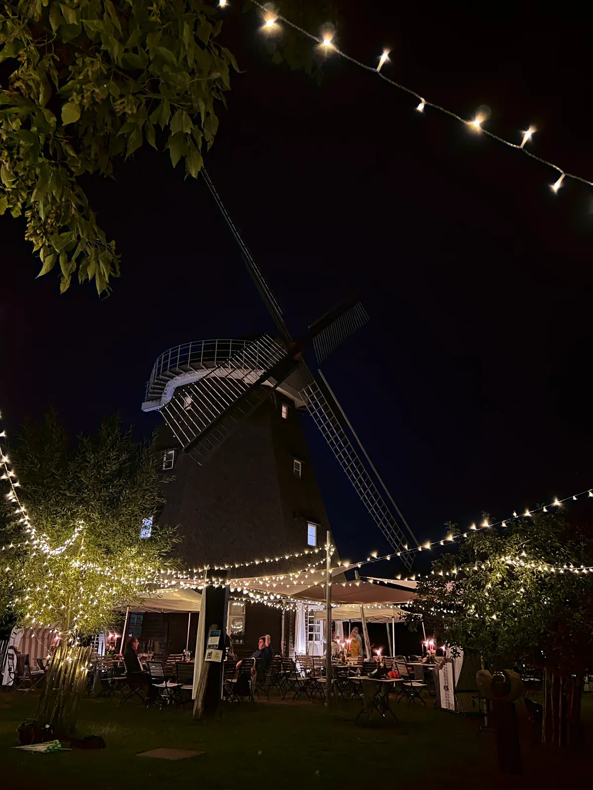 Abendlicher Blick durch Lichterketten auf die Mühle zwischen beleuchteten Bäumen