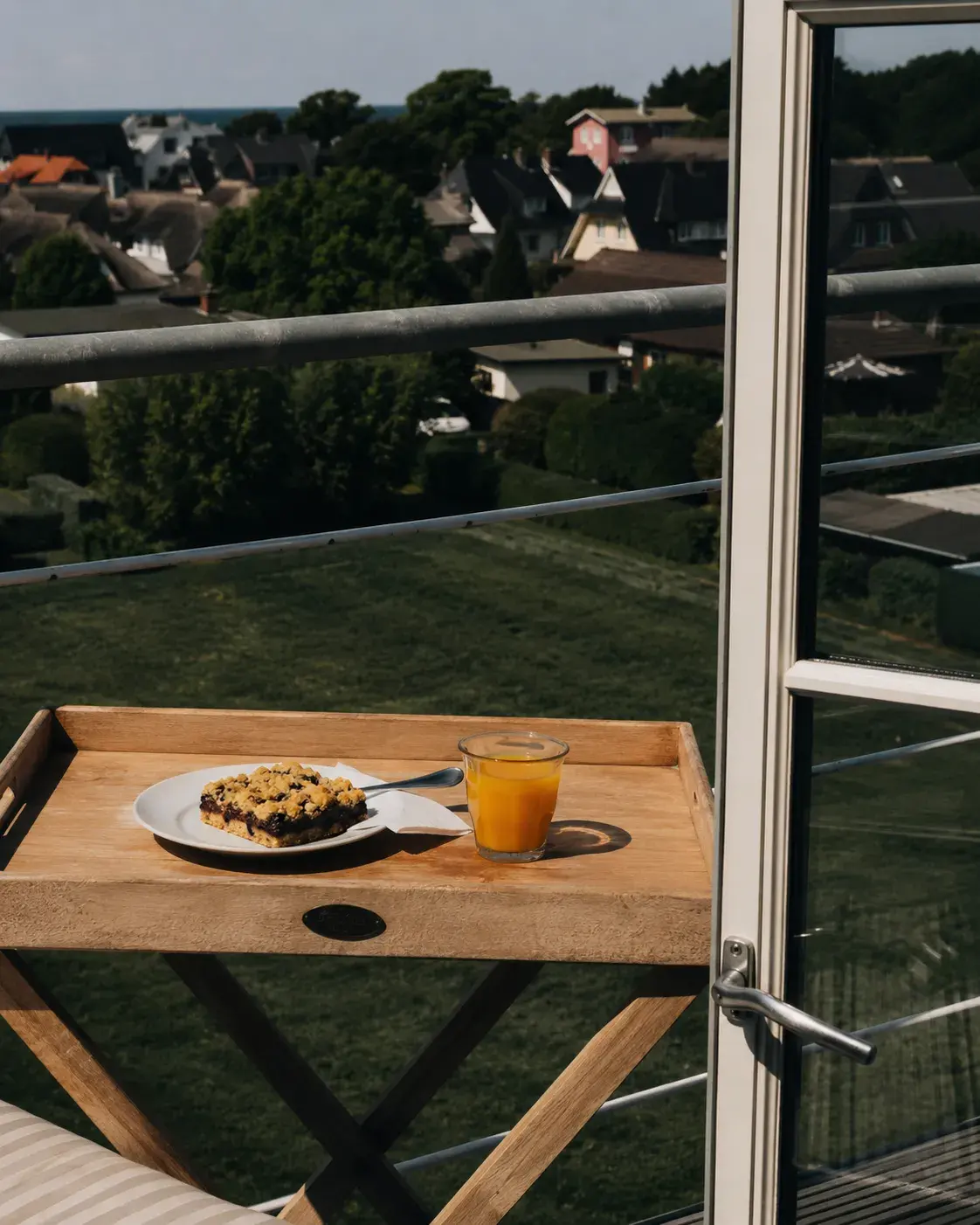 Frühstückstablett mit Kuchen und Saft auf der Mühlengalerie, dahinter der Blick über Ahrenshoop zur Ostsee