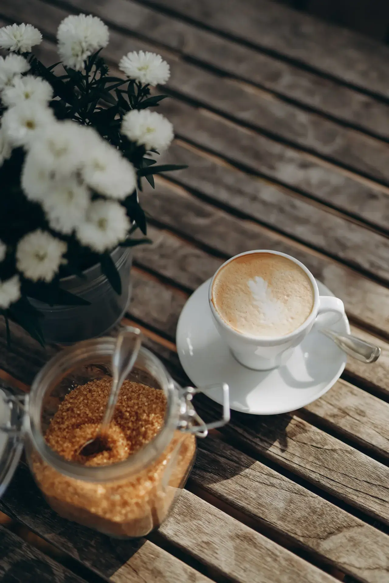 Cappuccino mit weißen Blumen und braunem Zucker